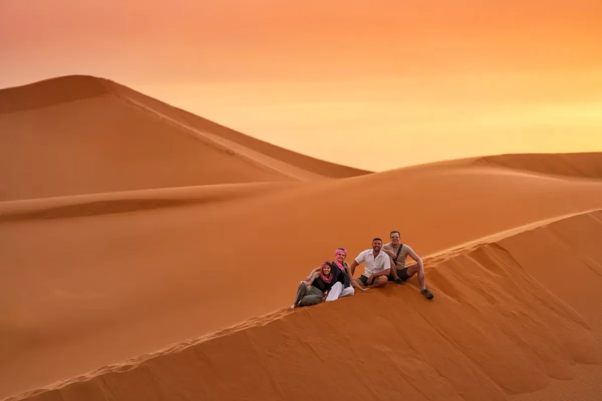 Vier reizigers zitten op een rode zandduin bij zonsondergang