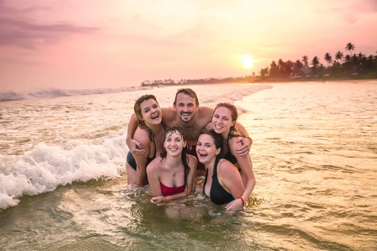 Vrienden lachen samen in de golven bij zonsondergang